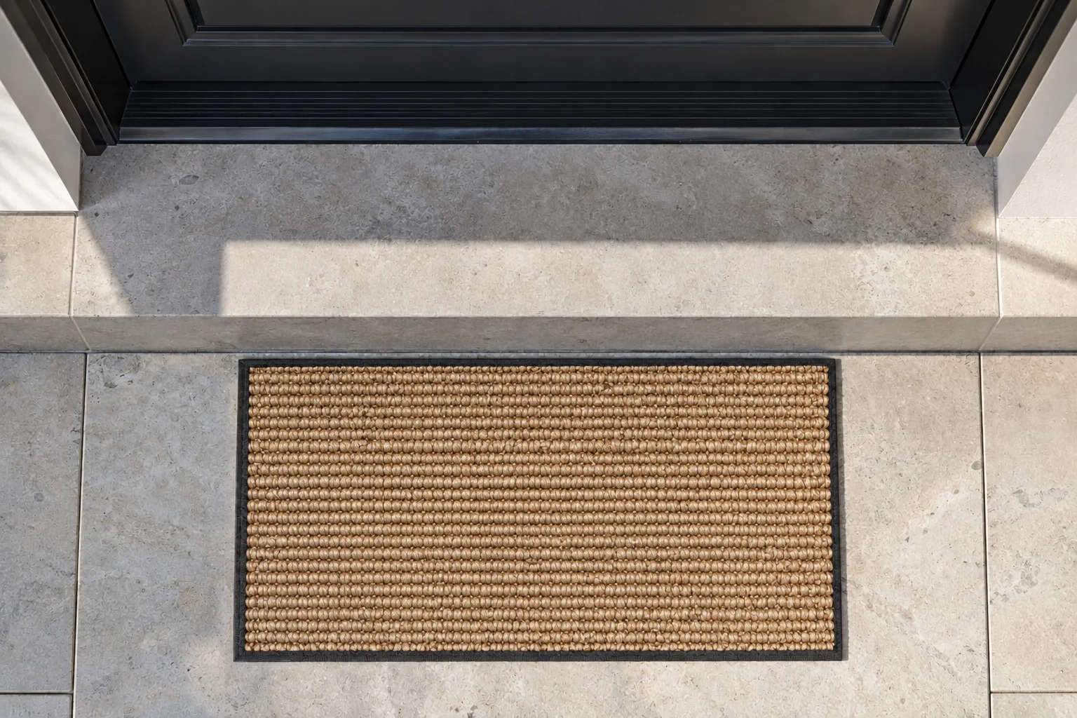 A coir doormat set into a stone threshold beneath a dark front door