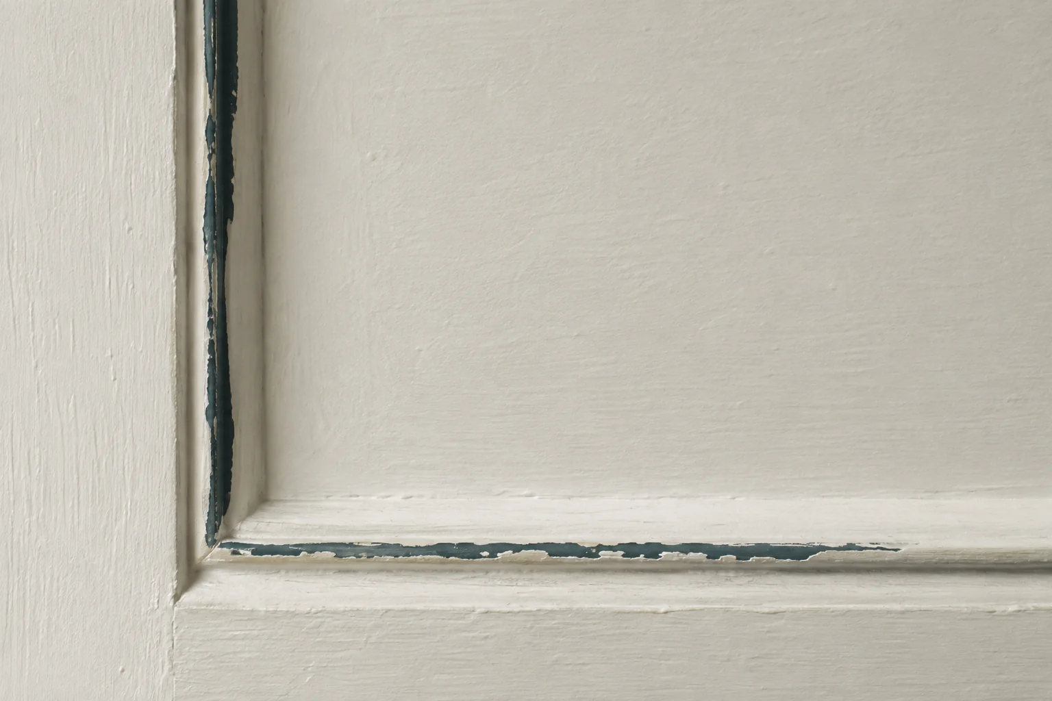 A painted white door panel where the old dark teal paint shows through along the edges