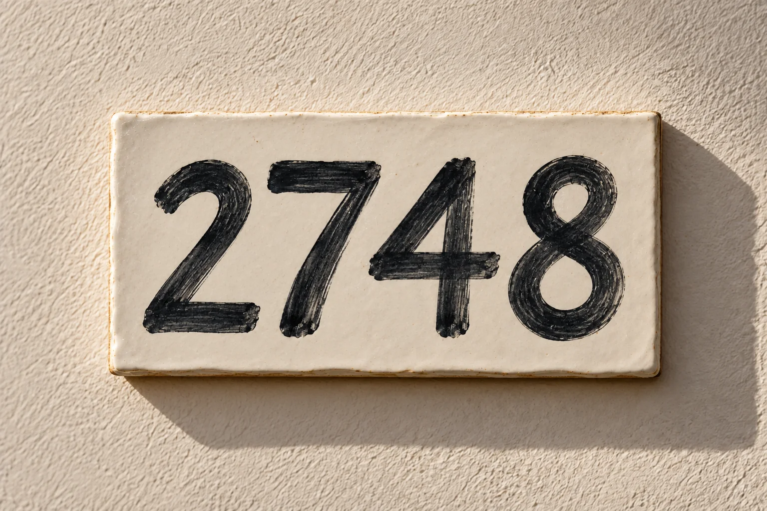 A hand-painted ceramic house number tile reading 2748, mounted on a textured wall