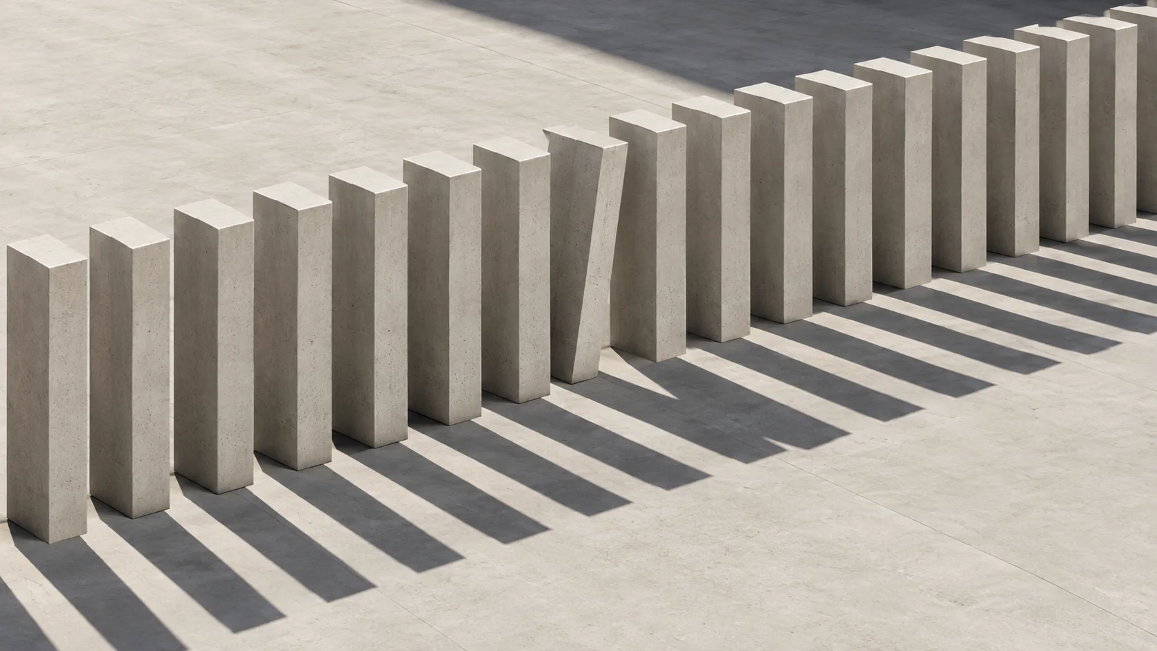 A row of identical upright concrete blocks casting parallel shadows, with one leaning out of line