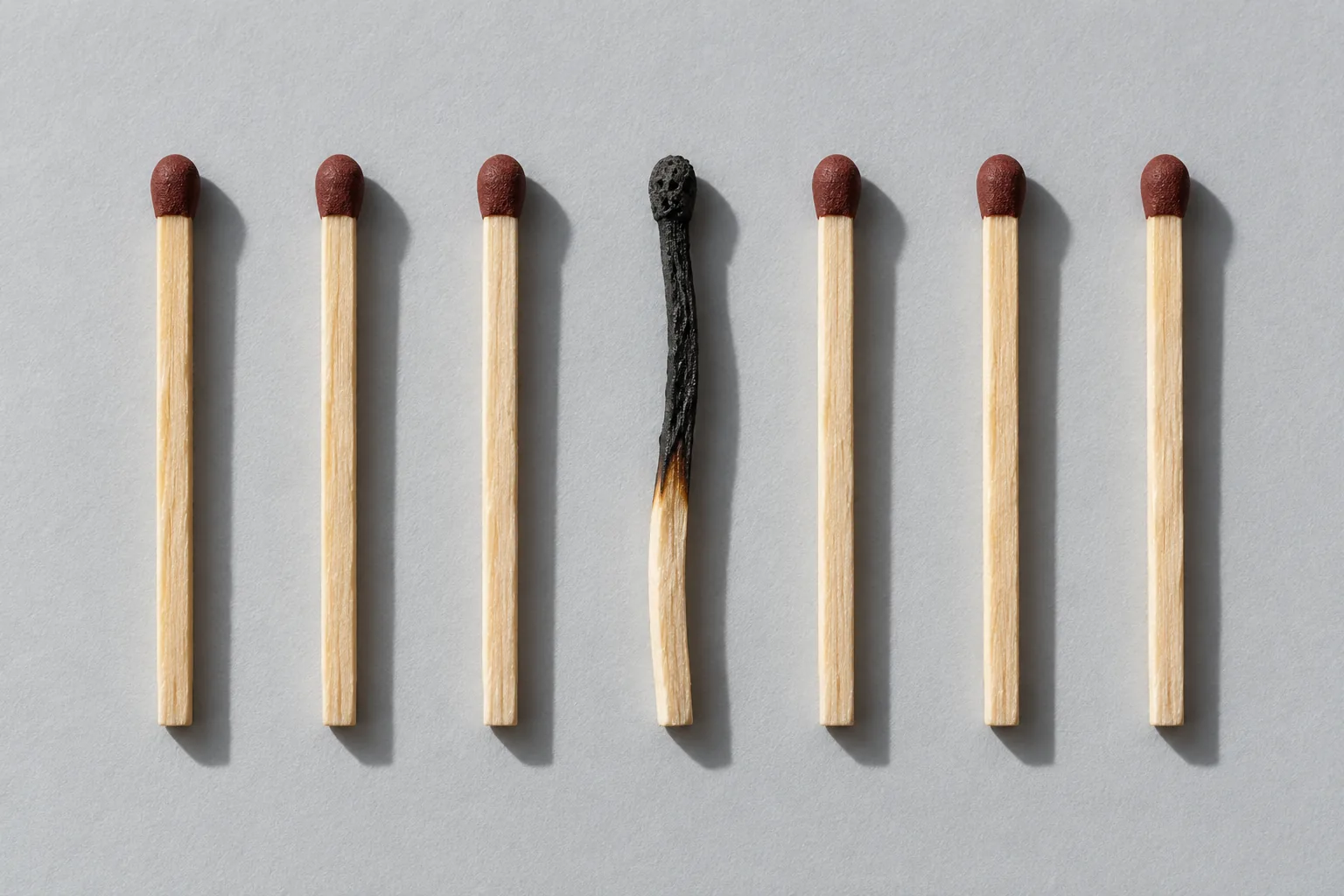 Seven wooden matches laid in an evenly spaced row, the middle one burnt black and buckled