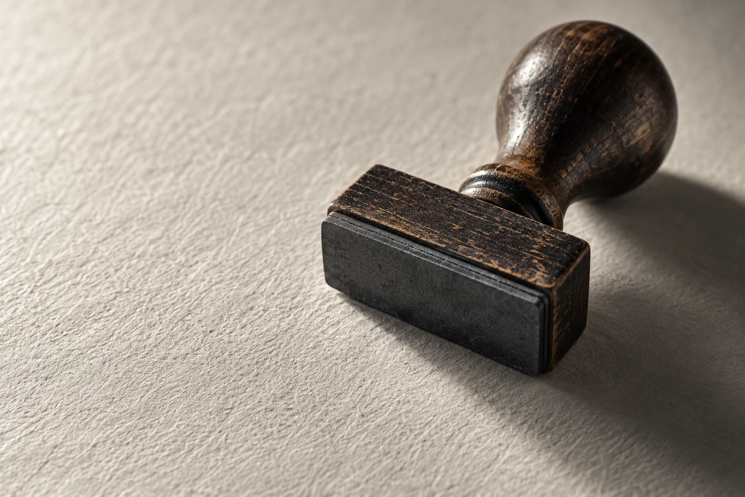 A wooden rubber stamp resting on textured paper, lit from one side